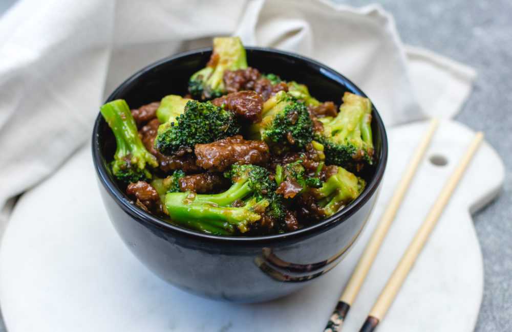 beef chunks and broccoli florets with sauce in a black bowl with chopsticks on the side