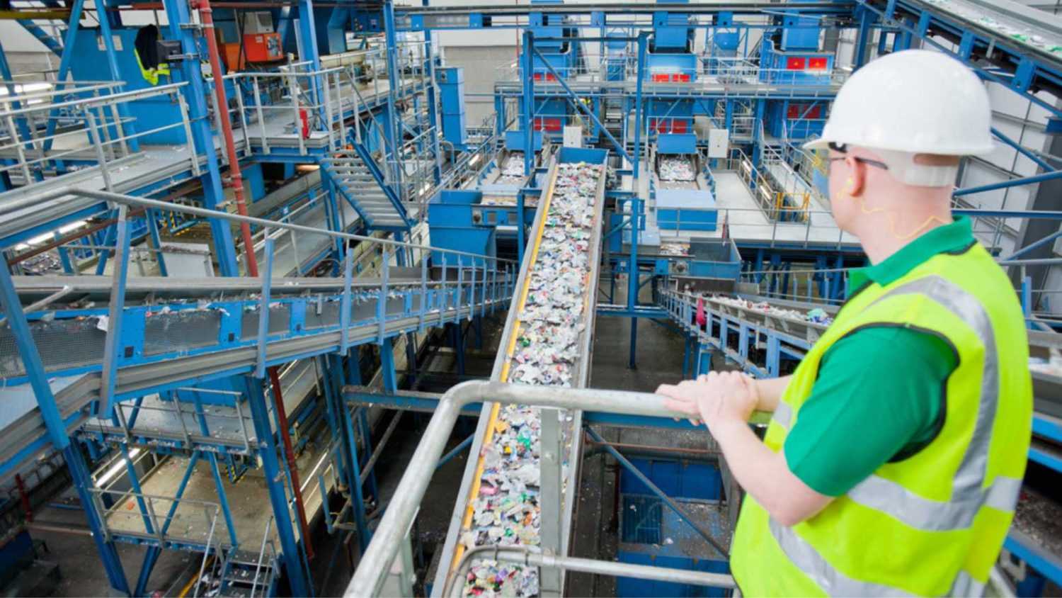 Worker observing plastic on conveyor belt in recycling plant
