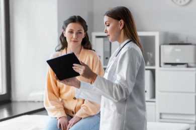 medicine, healthcare and people concept - female doctor with tablet pc computer talking to woman patient at hospital