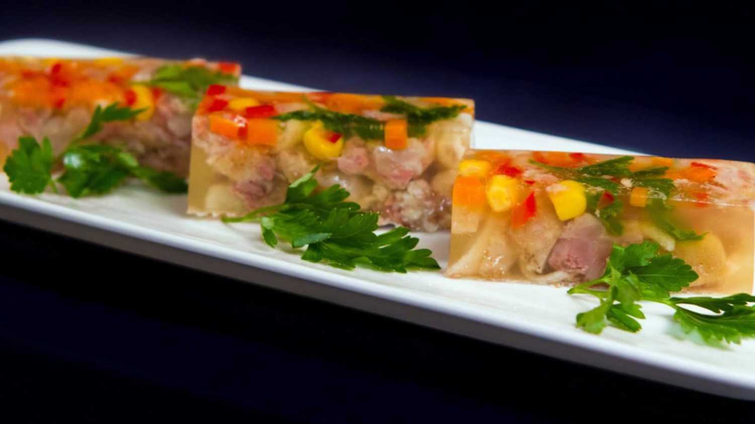 cubes of aspic with boiled meat, paprika, carrots and maize corn, served with parsley on black background, detail close-up