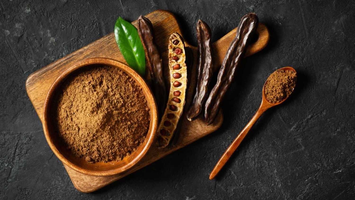 Carob bean and powder on board flat lay on black background, top view, copy space