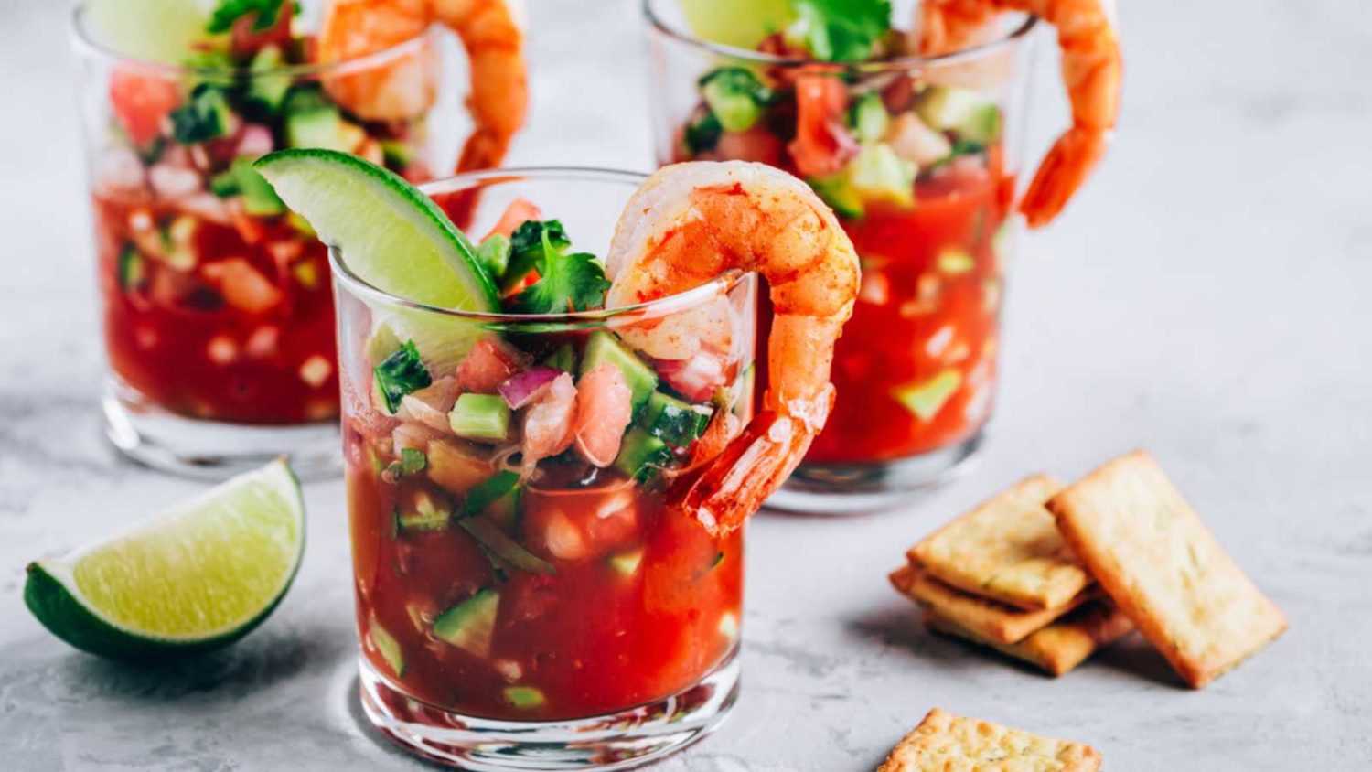 Refreshing Mexican Shrimp Cocktail with lime in glass on gray stone background, copy space.