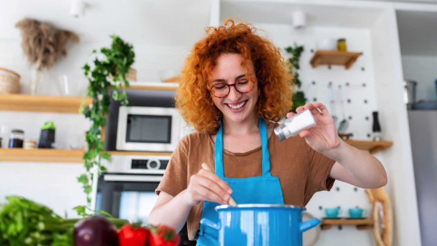 Woman preparing soup adding salt
