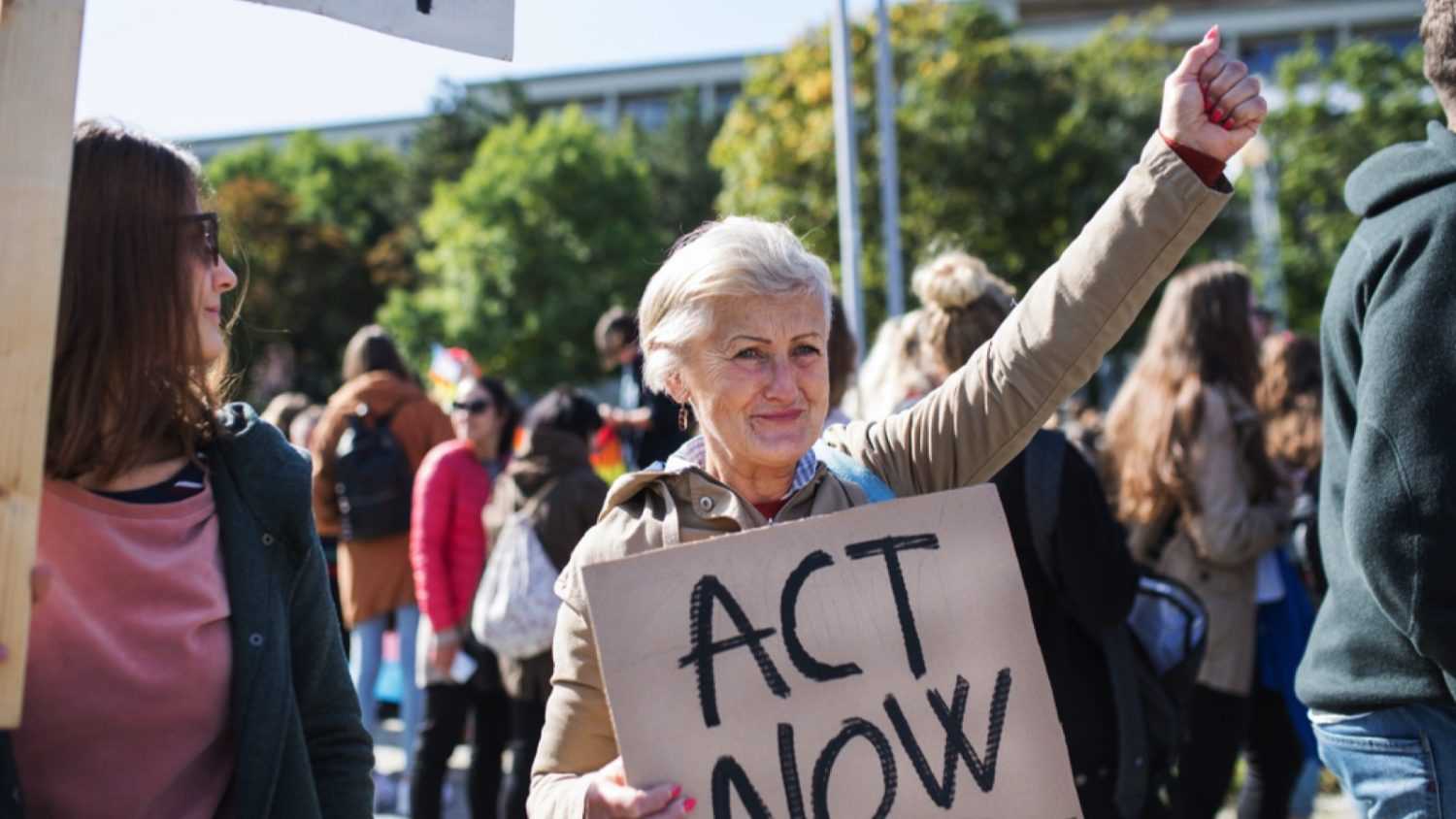 Old woman holding board participating in rally